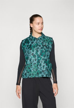Gilet à imprimé léopard vert et noir, avec un col et une fermeture éclair à l'avant, fabriqué dans un tissu lisse, associé à un haut à manches longues noir.