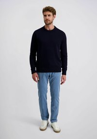 Marineblauer gestrickter Pullover mit Rundhalsausschnitt, kombiniert mit hellblauen gestreiften Hosen und weißen Sneakern mit beige abgesetzten Sohlen.
