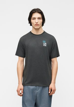 Giovane con capelli scuri fino alle spalle che indossa una t-shirt grigio scuro O'Neill con un piccolo logo di palma sul petto e jeans blu.
