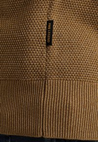 Brązowy sweter o fakturze z plecionym wzorem, z prążkowanym dołem i czarną metką z haftem "PME LEGEND" po boku.