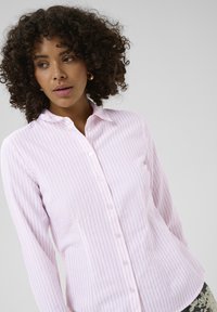 Chemise boutonnée à rayures roses et blanches, avec manches longues, col et silhouette ajustée. Texture de tissu lisse.