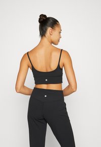 Czarny sportowy crop top z cienkimi ramiączkami, gładką fakturą i logo. Połączony z czarnymi legginsami o wysokim stanie z dopasowanymi detalami.