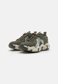 Des chaussures de sport vertes avec un dessus texturé, des accents argentés, une semelle blanche épaisse et un design à lacets avec une languette au niveau du talon.