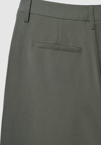Pantalon vert olive avec une texture lisse, comportant une poche arrière unique et un design ajusté. La taille est dotée d'passants de ceinture.
