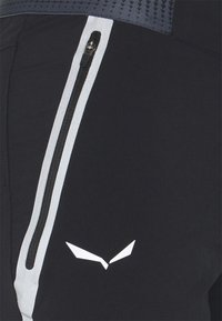 Černé sportovní šortky s boční kapsou na zip, bílými akcenty a výrazným logem. Hladká látka s texturovaným designem pasového lemu.