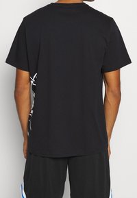 Czarny bawełniany t-shirt z krótkimi rękawami, z białym nadrukiem graficznym po lewej stronie. Prosty krój i klasyczny okrągły dekolt.