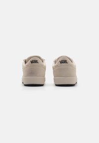 Beige Wildledersneaker mit glatter Oberfläche, runder gepolsterter Schuhkragen und schwarzem Logo an der Ferse. Gummisohle mit strukturiertem Grip.