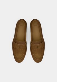 Mocasini maro din piele întoarsă, cu vârf rotund, bandă pe partea superioară și un branding subtil. Textură netedă cu un finisaj uniform.