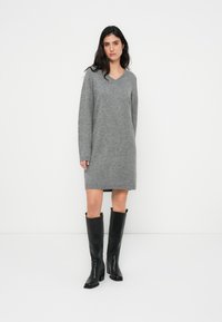 Γκρι πλεκτό φόρεμα με V-λαιμόκοψη, μακριά μανίκια και ευθεία σιλουέτα. Συνδυάζεται με ψηλές μαύρες δερμάτινες μπότες, με χοντρό τακούνι.