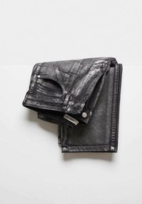 Vaqueros negros con acabado brillante, con diseño de cinco bolsillos, herrajes plateados y detalles de costuras visibles, doblados cuidadosamente sobre una superficie blanca.