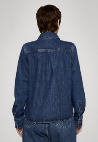 Kurtka dżinsowa w ciemnym niebieskim kolorze z klasycznym kołnierzem, zapinanymi na guziki mankietami i szwem na tylnej części. Charakteryzuje się luźnym krojem i miękką teksturą.