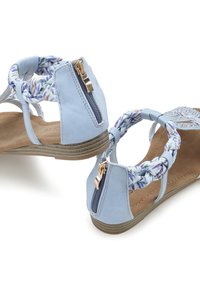 Blauer Sandale mit geflochtenen Blumenriemen, Reißverschluss und gemustertem Fußbett. Sie verfügt über eine flache Sohle mit strukturiertem Gummiboden.