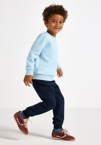 Lichtblauwe langemouwen sweatshirt met geribde manchetten, gecombineerd met marineblauwe sweatpants. Bruine en rode sneakers met beige veters en accenten.
