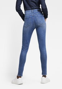 Jeans ajustados de denim en color azul, con una cintura alta, cinco bolsillos y detalles de costura sutiles. Combinados con zapatillas blancas.