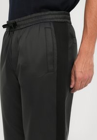 Sorte lette joggebukser med elastisk midje, sidelommer og kontrasterende svarte striper langs sidene. Glatt tekstur.