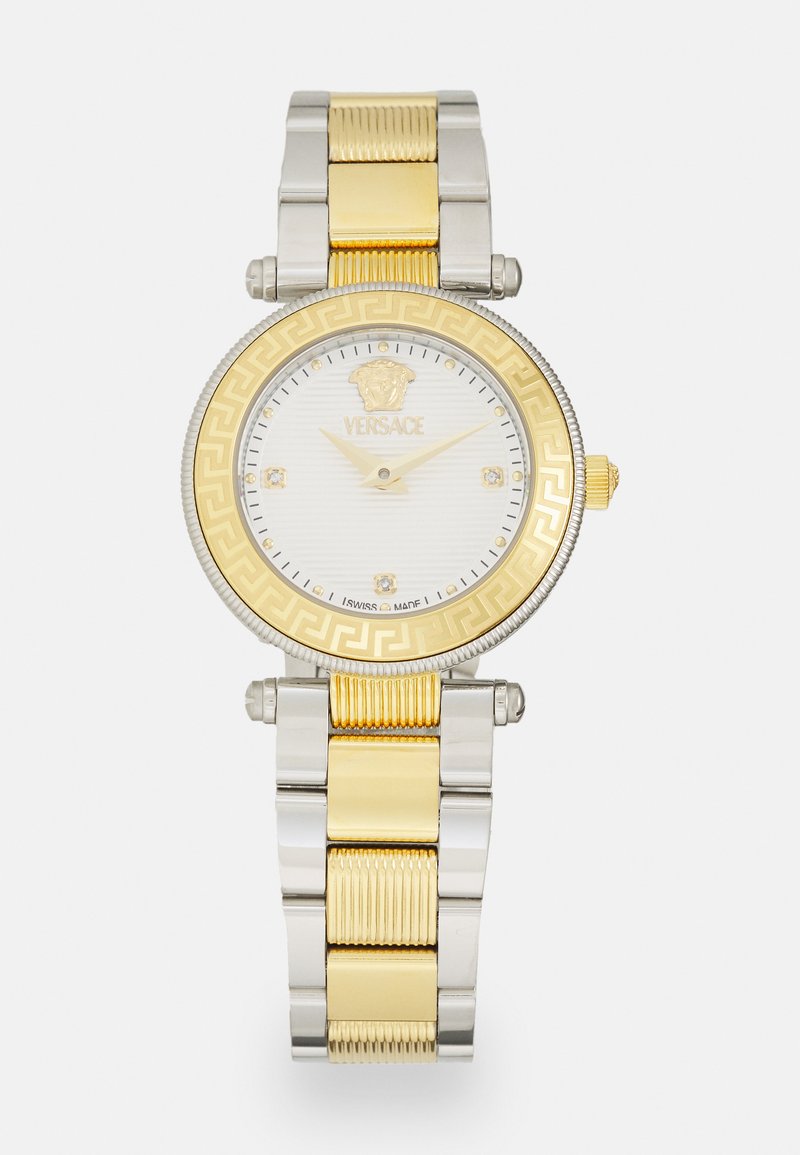Relógio Versace com uma bracelete metálica prateada e dourada, mostrador redondo branco, bezel dourado com um padrão de chave grega e diamantes nos marcadores de horas.