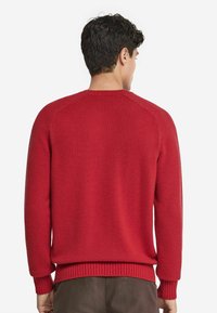 Röd stickad tröja med rund halsringning, ribbade ärmslut och fåll, samt en mjuk textur. Klassisk passform med raglanärmar.