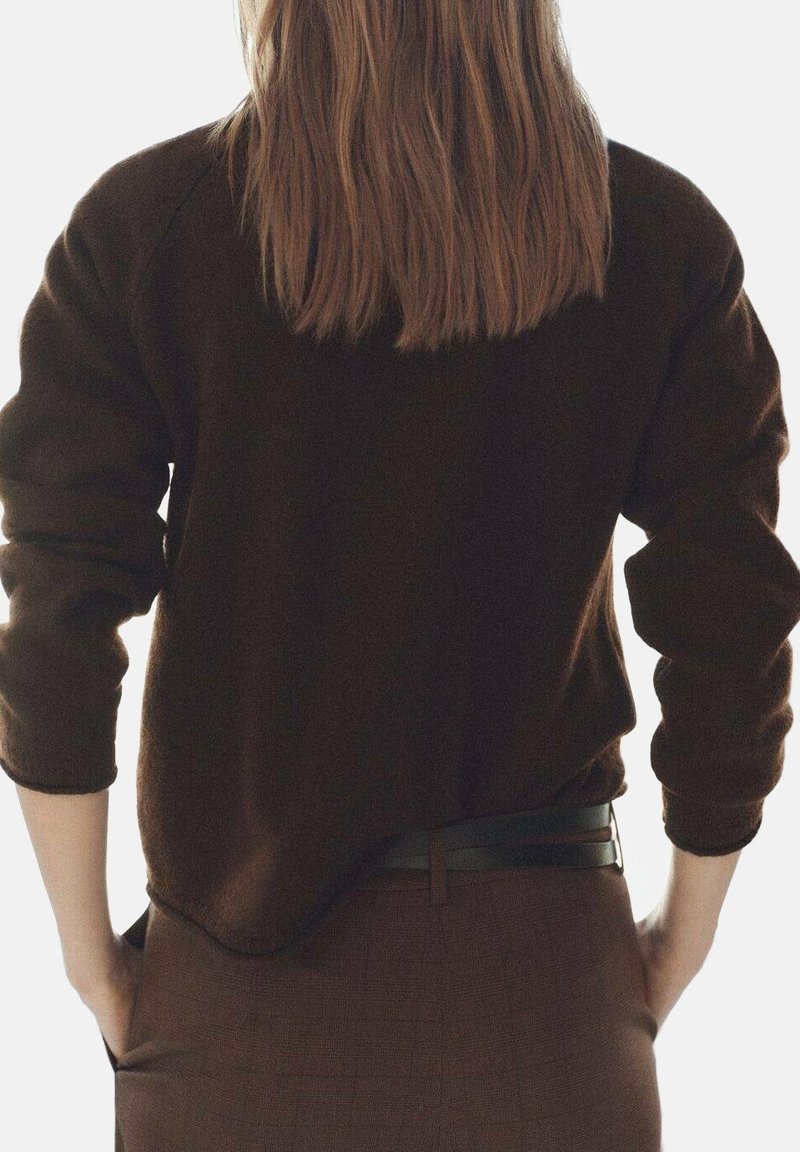 Maglione marrone lavorato a maglia con una vestibilità rilassata, polsini a coste e una texture morbida, indossato con una gonna marrone aderente e una cintura nera.