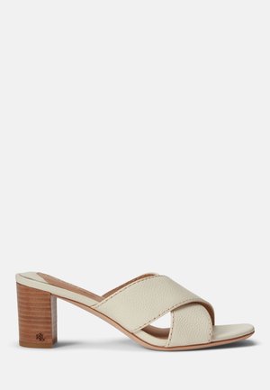 Mule beige à bout ouvert avec larges brides en cuir croisées et talon bloc en bois empilé.