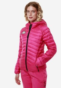 Giacca a vento rosa con trapuntatura orizzontale, dotata di cappuccio, zip nera e logo Kappa. Tessuto liscio e lucido con due tasche laterali.