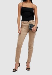 Beige cargobyxor med flera fickor, slim fit, fransad fåll, kombinerade med en svart ärmlös topp och svarta högklackade sandaler.