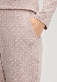 Pyjamastel in lichtroze met een bladenpatroon. De stof is zachte katoen, met een zak en decoratieve stiksels nabij de zoom.