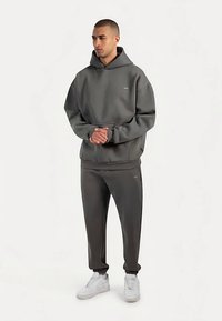 Sudadera con capucha gris y pantalones deportivos a juego hechos de tela suave y texturizada. Incluye un bolsillo frontal y puños acanalados, combinados con zapatillas blancas.