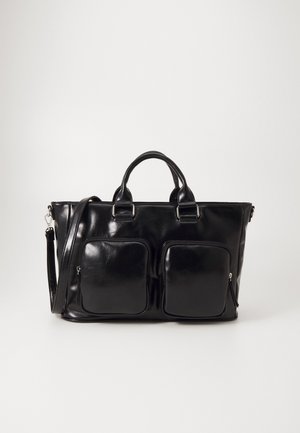 Sac fourre-tout en cuir noir avec deux poignées supérieures, bandoulière amovible et deux poches avant zippées sur un fond clair uni.