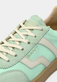 Αθλητικά παπούτσια σε χρώμα μέντας με σουέτ και υφασμάτινα υλικά, λευκά κορδόνια, μπεζ λεπτομέρειες και χρυσό λογότυπο "GANT" στο πλάι.