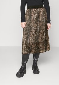 Svart långärmad topp kombinerad med en veckad knälång kjol med ett metalliskt djurmönster i brunt och svart, bärs med svarta klumpiga stövlar.