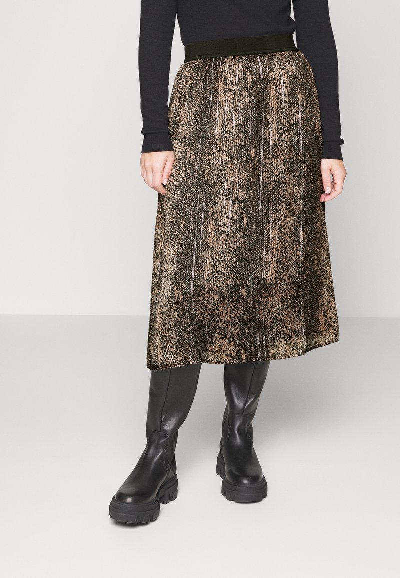 Svart långärmad topp kombinerad med en veckad knälång kjol med ett metalliskt djurmönster i brunt och svart, bärs med svarta klumpiga stövlar.