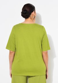 T-shirt in cotone verde con maniche corte, scollatura rotonda e vestibilità rilassata. Indossato con pantaloni abbinati, visto da dietro su uno sfondo bianco.