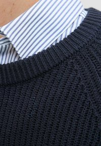 Navy knitted sweater featuring a ribbed texture, paired with a light blue and white striped collared shirt.