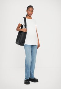 Camiseta blanca de canalé con dobladillo en forma de ola, jeans acampanados azules y bolso negro de hombro. Unos zapatos de plataforma negros completan el conjunto.