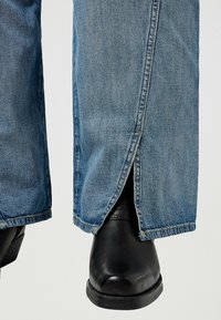 Blå denimjeans med rak skärning och sidofickor, parat med svarta läderankelboots. Tyget är lätt texturerat.