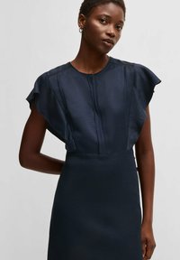 Marinblå klänning med korta volangärmar, slät textur och vertikala framveck. Enkel design utan mönster eller synlig hårdvara.