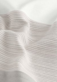 Tissu doux et côtelé avec des bandes horizontales texturées alternées en gris clair et blanc, présenté en plis doux.