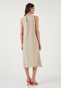 Beige, sleeveless midi dress with a textured fabric, gathered neckline, and a keyhole back. Paired with multi-colored heeled sandals.