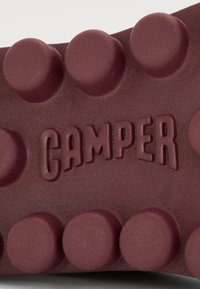 Bordo gumeni potplat cipele s uzdignutim kružnim uzorcima i utisnutim logotipom "CAMPER", s teksturiranim površinom za bolji zahvat.