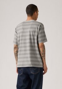 Gråstripete kortermet skjorte laget av myk stoff, med en avslappet passform og en klassisk rund hals, brukt sammen med mørke denimjeans.