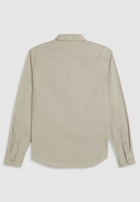 Chemise à manches longues en tissu beige clair. Présente un col pointu, des poignets boutonnés et un ourlet arrondi. Texture lisse sans motifs.