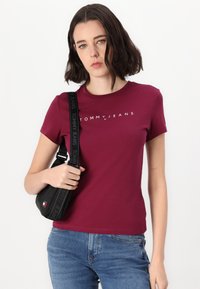 Marooni puuvillane T-särk lühikeste varrukatega, millel on valge "TOMMY JEANS" logo. Komplektsus musta kotiga, millel on bränditud rihm ja väike logo.