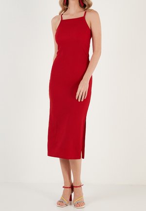 Robe midi rouge côtelée avec bretelles spaghetti ajustables et fente latérale, associée à des sandales à brides multicolores. Texture de tissu lisse.