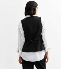 Svart linväst med en figursydd design, med en detalj av baksidan som knyts. Bärs över en vit skjorta, vilket framhäver en ren, minimalistisk stil.