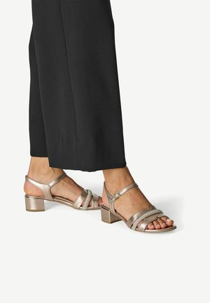 Sandales à talons blocs métalliques dorées avec brides croisées et bride de cheville réglable, présentant une texture lisse et un design à bout ouvert.