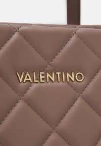 Kvartets brūns ādas rokassomu, kurai ir zelta "VALENTINO" logotips. Virsma ir gluda ar smalku šuvju detaļām.