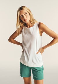 Top senza maniche bianco con la scritta "FREDDY" in grigio, abbinato a pantaloni corti verdi. Il tessuto sembra morbido con una vestibilità rilassata.