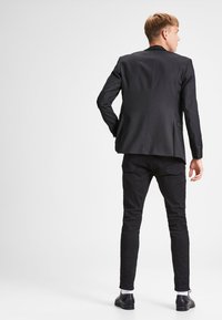 Dark gray blazer with a tailored fit, single back vent, paired with slim black trousers. Smooth fabric, minimalistic design, subtle stitching.