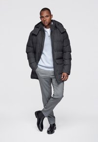 Grå vadderad jacka med huva, ljusgrå tröja, grå byxor och svarta fotkängor. Texturerat tyg med synliga sömmar och fickor.