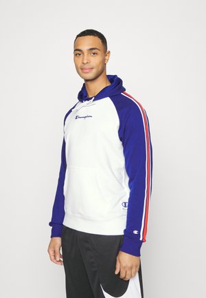 Sudadera con capucha en blanco y azul con rayas rojas. Cuenta con un bolsillo tipo canguro y un logo. La tela parece suave con un diseño de color contrastante.